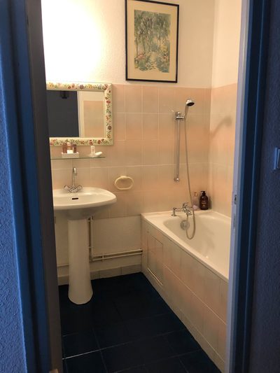 Salle de bains de Campanule : murs bleus, baignoire, lavabo sur colonne et miroir encadré.