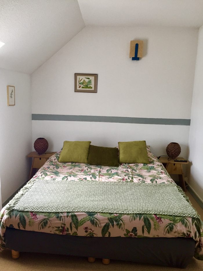 Chambre Fougère : lit queen size sous rampant, parure à motif de feuillages, deux chevets en bois et petites gravures encadrées.